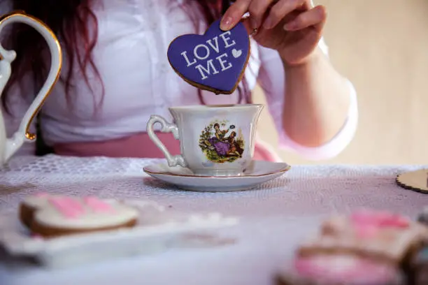 Midsection of a woman dipping heart-shaped cookie into tea. Mix of retro and modern style.