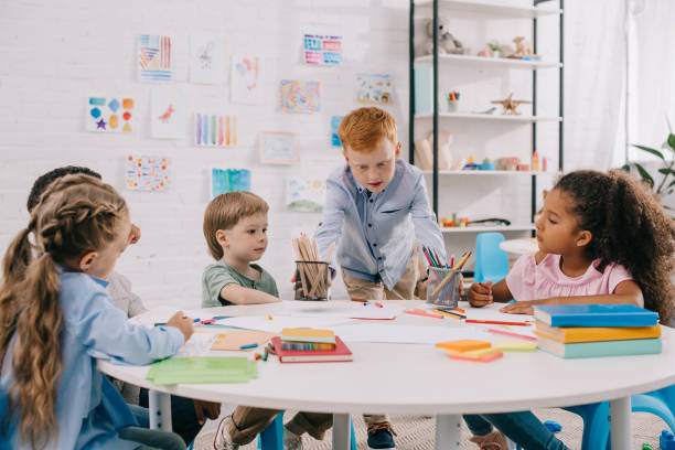 istock interracial kids sitting at table with papers and paints for drawing in classroom 1015998228