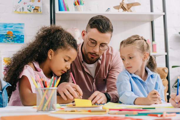 istock teacher in eyeglasses helping multicultural preschoolers with drawing at table in classroom 1015998514