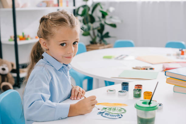 istock side view of cute child sitting at table with paints and paint brushes 1015998622