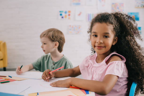 istock selective focus of multicultural preschoolers at table with papers and pencils in classroom 1015998930