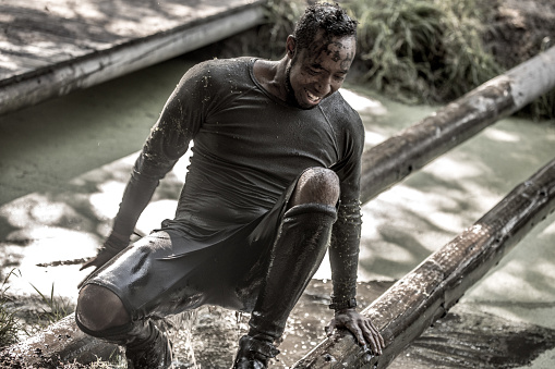 Individual young black man having sporty fun at a public mud run obstacle course