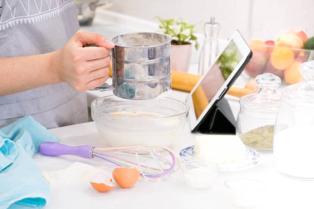 istock Closeup hands lady standing in kitchen and cooking the dough. Looking at tablet computer. Female following recipe on digital cooking healthy meal. Retro look 1016006086