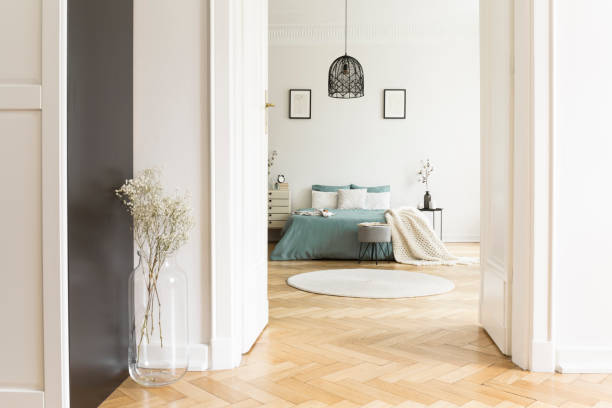 istock Open door to white bedroom interior with herringbone parquet, king-size bed with pillows and knit coverlet, round rug and simple posters 1016014220