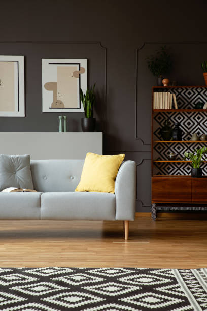 istock Yellow pillow on grey couch in retro living room interior with patterned carpet and posters. Real photo 1016018116
