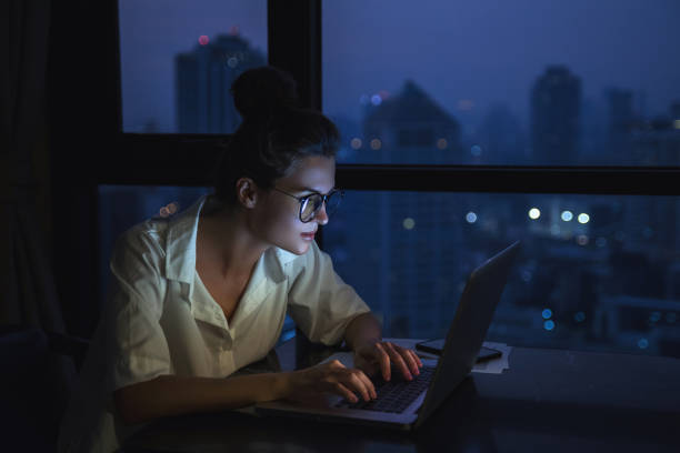 Woman is working with laptop at home during night.