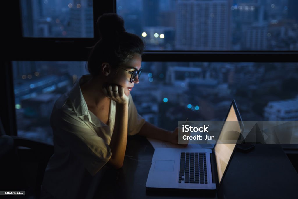 Woman is working with laptop at home during night. Overtime concept. Woman is working with laptop at home during night. Night Stock Photo