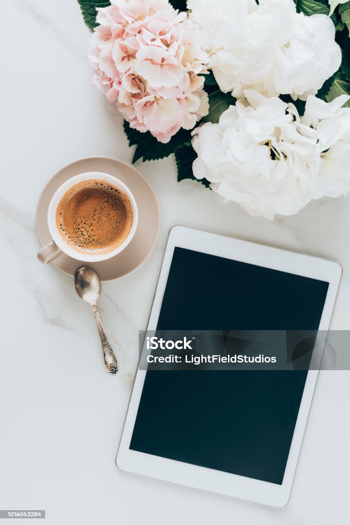 top view of cup with espresso coffee, hortensia flowers and digital tablet with blank screen on marble surface Digital Tablet Stock Photo