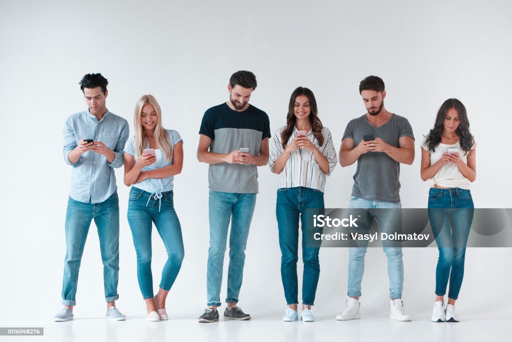 Group of young people on white background Group of young people isolated on white background. Attractive youth standing together with smart phones in hands. Technology concept. Group Of People Stock Photo