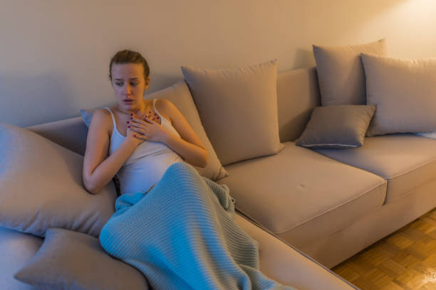 mujer joven en pijama con ataque al corazón en su sala de estar - human hand help pain heart attack fotografías e imágenes de stock