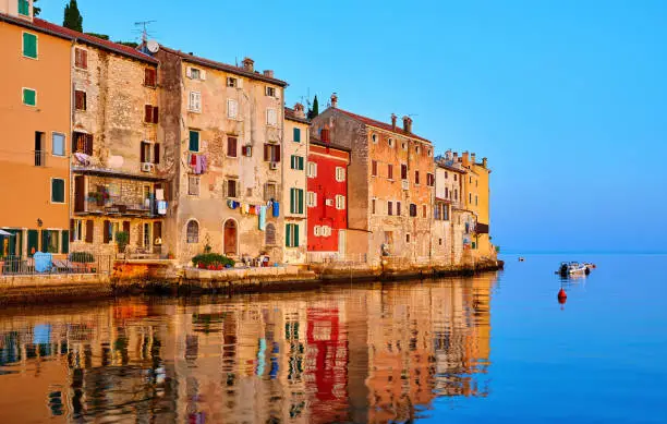 Rovinj, Istria, Croatia. Antique medieval houses at coastline of Adriatic sea. Sunrise with blue sky and fishing boat on horizon. Calm and silent summer morning.