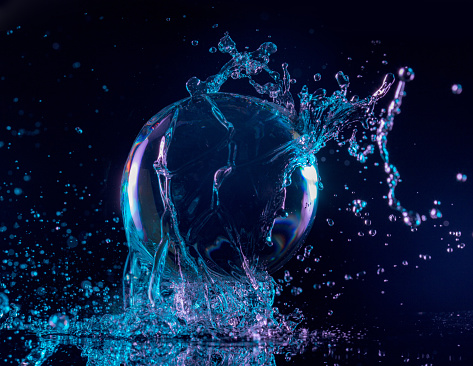 blue and purple water splashing over a transparent ball in a dark background