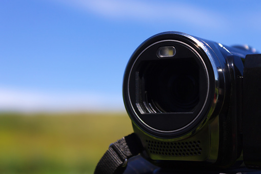 Camera lens during filming against the background of a green meadow and clear sky on a summer day