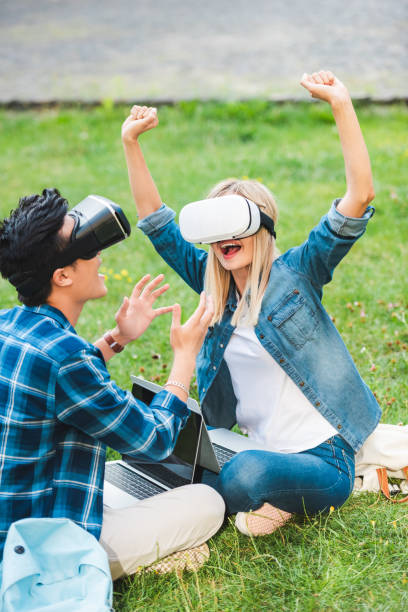 istock side view of multicultural students in virtual reality headsets with laptops sitting on green grass in park 1016087508