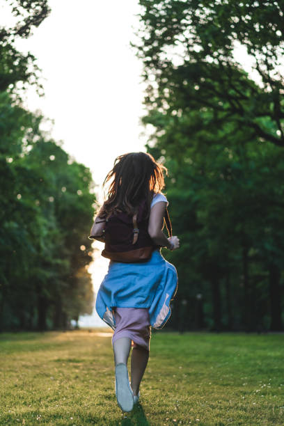 istock rear view of woman with backpack running on meadow with trees 1016102544