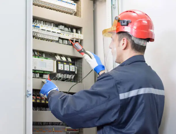 Tehnician with red hardhat testing equipment in electrical room