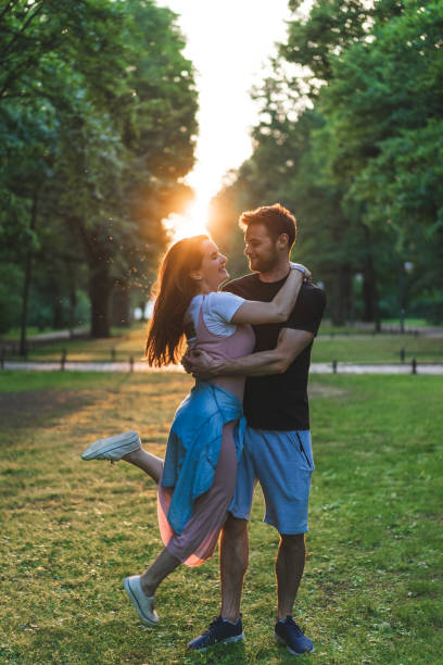 istock young man holding happy girlfriend with closed eyes in park with setting sun behind 1016102602