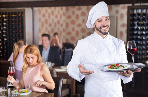 Portrait of confident smiling chef standing with serving tray at a restaurant