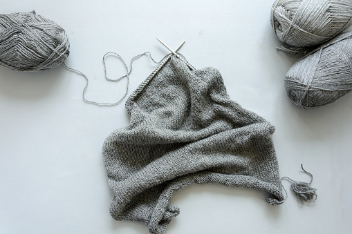 Girl knits gray sweater knitting needles on gray wooden background. Process of knitting. Top view. Flay lay