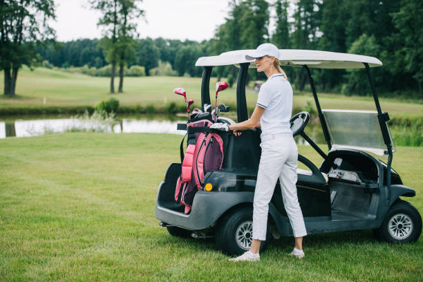 femme polo et casquette avec golf gear debout au chariot de golf au terrain de golf le jour de l’été - golf cart golf mode of transport transportation photos et images de collection