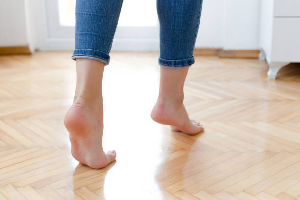 Bare Foot Standing on Wooden Floor Background, Top View. Selfie of Woman Bare Feet and Leg on Wood. Cropped Image of Beautiful Young Female Body Legs with Fingernail on Brown Pedicure and Manicure.