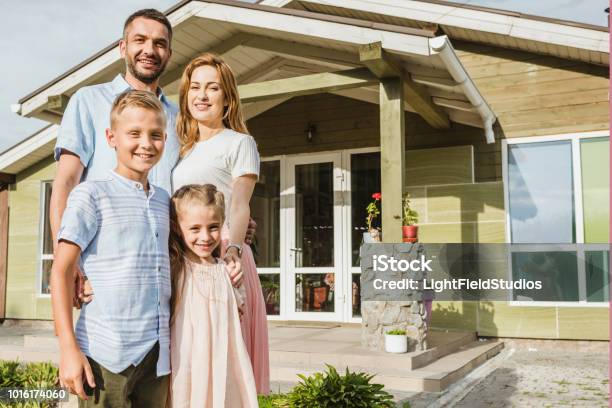 Smiling Parents And Children Standing In Front Of House Stock Photo - Download Image Now