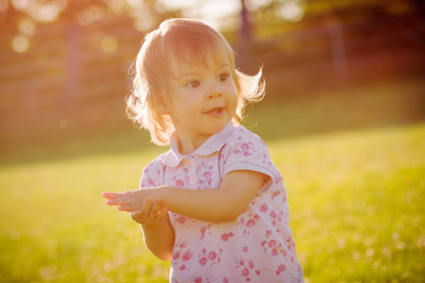 Cute adorable baby girl is playing outdoors at sunset light.