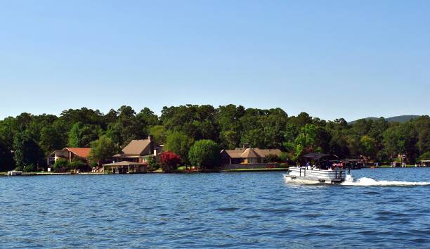 Lake House on the Lake with a Pontoon Boat in the Water Beautiful scenic view of lake houses on the shoreline with a pontoon boat in the water. pontoon boat stock pictures, royalty-free photos & images