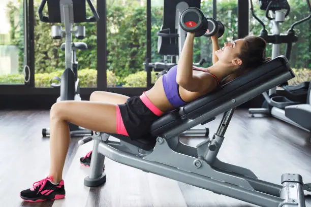 Young and beautiful woman working out with dumbbells in gym. Incline bench press exercise.