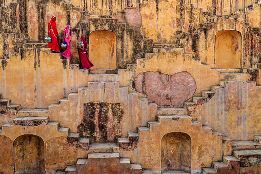 Indian women carrying water from stepwell near Jaipur, Rajasthan, India. Women and children often walk long distances to bring back jugs of water that they carry on their head. 
Stepwells are wells in which the water may be reached by descending a set of steps.