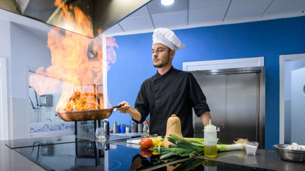 young chef vegetables flamed with fire in a frying pan, side view stock photo