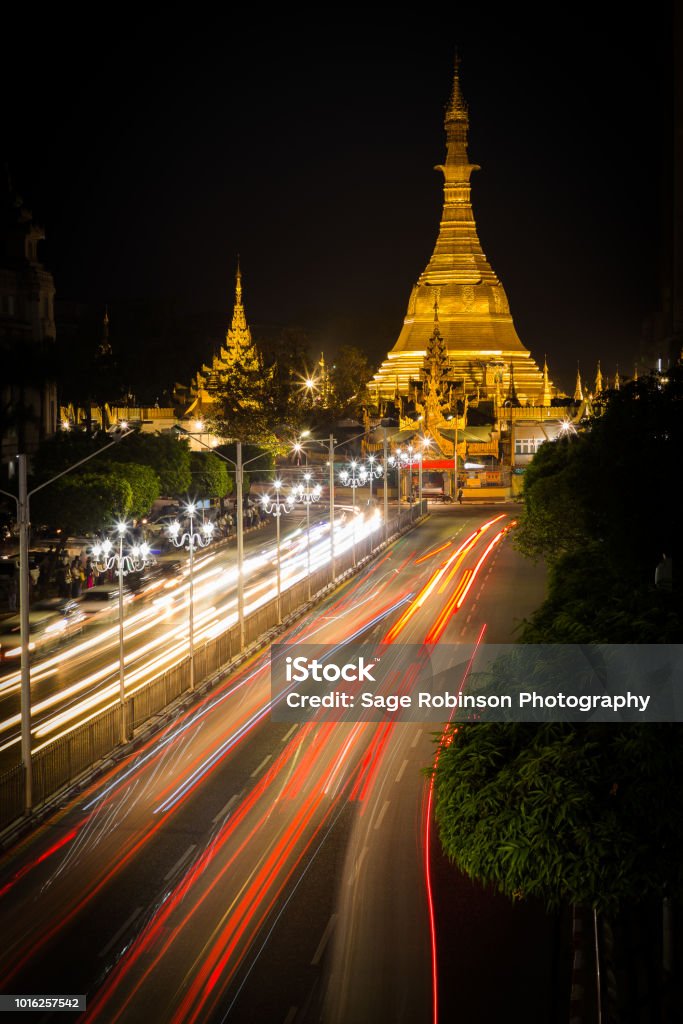 Sule Pagoda by night in downtown yangon. Brightly light golden pagoda with light trails from traffic in the foreground long exposure night landscape Architecture Stock Photo
