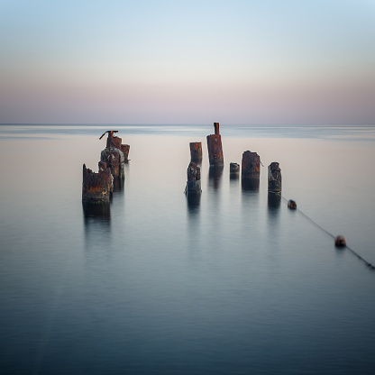 Long exposure. Piles stick out of the sea in the evening twilight. Square frame.