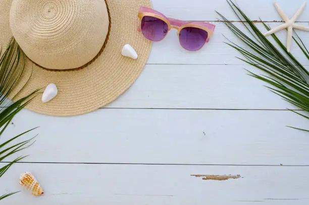 Photo of Beach relaxation board presentation with summer hat, sun glasses, palm leaves and sea shels on white planks background. Perfect for lettering.