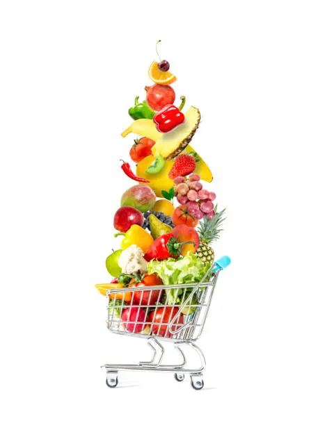 Photo of Fresh vegetables and fruits fly in a crowded shopping cart isolated on a white background. Mountain of fresh vegetables and fruits in a crowded shopping cart isolated on white background