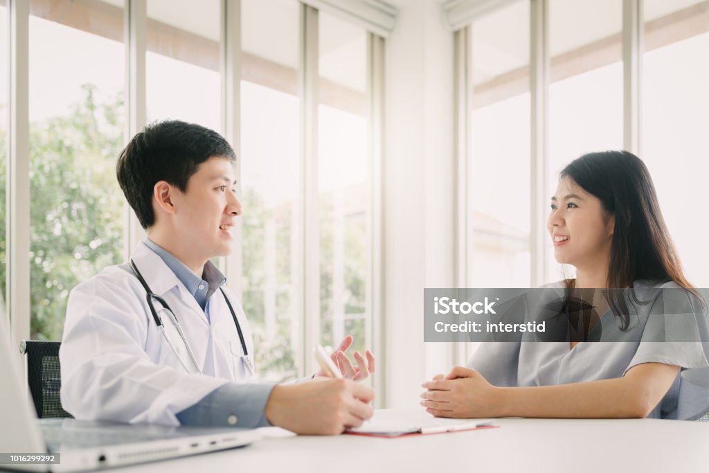 Doctor having consultation with female patient Asian doctor having consultation with young female patient in office Medical Exam Stock Photo