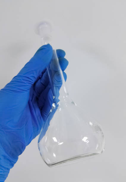 istock Volumetric glass flask and hand with blue safety glove. Isolated object. 1016307246