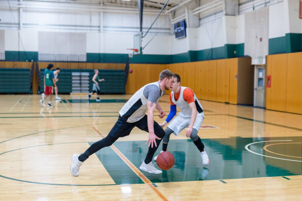 College Basketball Practice A college player plays 1-on-1 with his teammate, who is guarding him closely during a practice scrimmage They are both wearing practice jerseys. Others are practicing in the background. college basketball court stock pictures, royalty-free photos & images