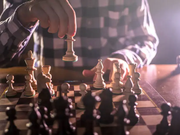 young male grandmaster hand making next move playing chess in dark place on a tournament