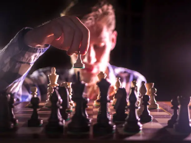 young male grandmaster hand making next move playing chess in dark place on a tournament