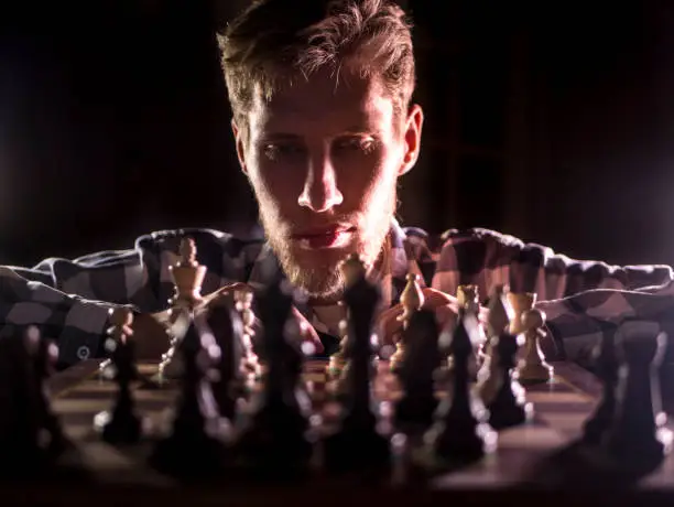 young bearded chess grandmaster sitting and thinking on the next move in dark room