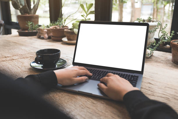 istock Mockup image of a woman using and typing on laptop with blank white desktop screen with coffee cup on wooden table in cafe 1016431950