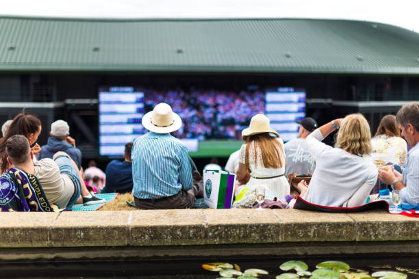 Crowd of people enjoying tennis on the hill, Wimbledon, UK Wimbledon, UK - 10 July, 2018: close up color image depicting crowds of spectators watching tennis on the big screen in Wimbledon, UK. Focus is on the rear view of tennis fans in the foreground, while the background of the big screen is blurred out of focus. wimbledon stock pictures, royalty-free photos & images