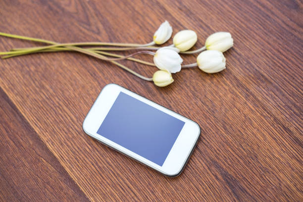 istock Mobile phone with white flowers on wooden background 1016459648