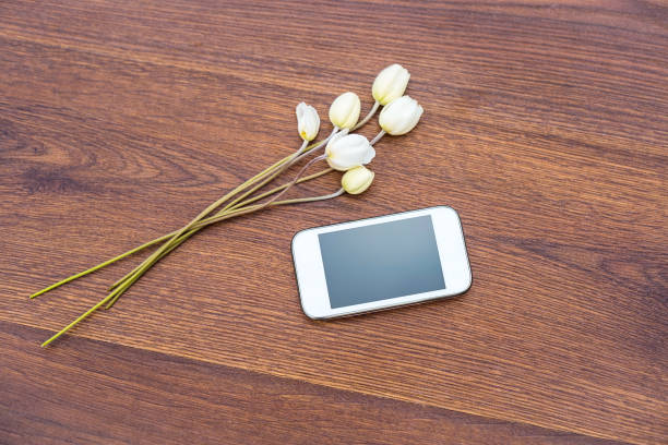 istock Mobile phone with white flowers on wooden background 1016459916