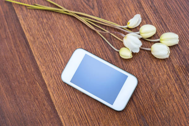 istock Mobile phone with white flowers on wooden background 1016462556