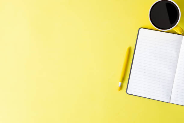 istock Home office desk with notebook paper, pen and coffee cup on yellow background top view mock up. 1016485036