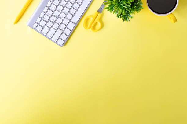 istock Office desk with computer keyboard, notebook paper, pen, coffee and plant decoration on yellow background top view mock up. 1016485684