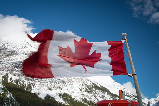 Canadian flag flying with blue sky and mountain in the background, on the boat to Spirit Island, Maligne Lake, Jasper National Park