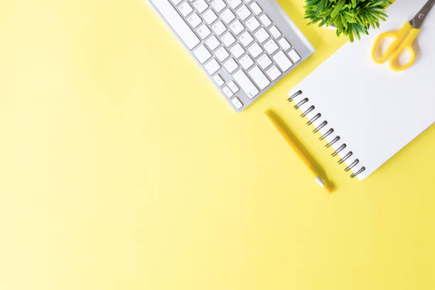 istock Above Office desk with computer keyboard, notebook paper, pen and plant decoration on yellow background top view mock up. 1016488242